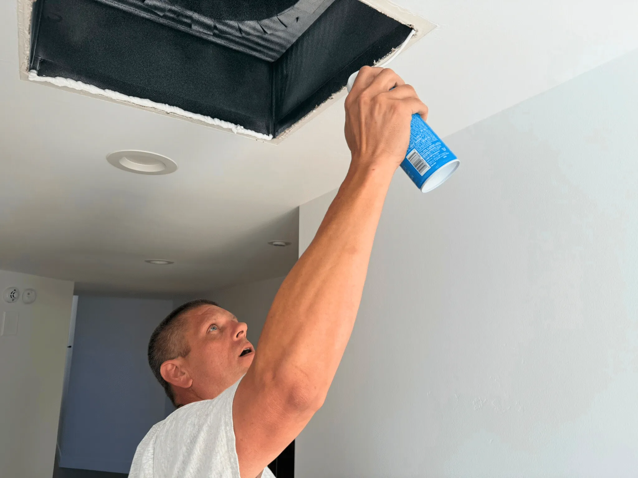 Mike With Blue Can applying spray foam for Building Performance Sealing around a ceiling vent