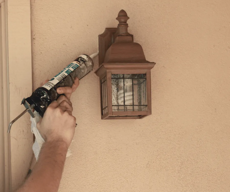 Technician applying caulk to a light fixture, highlighting sealing challenges in desert environments